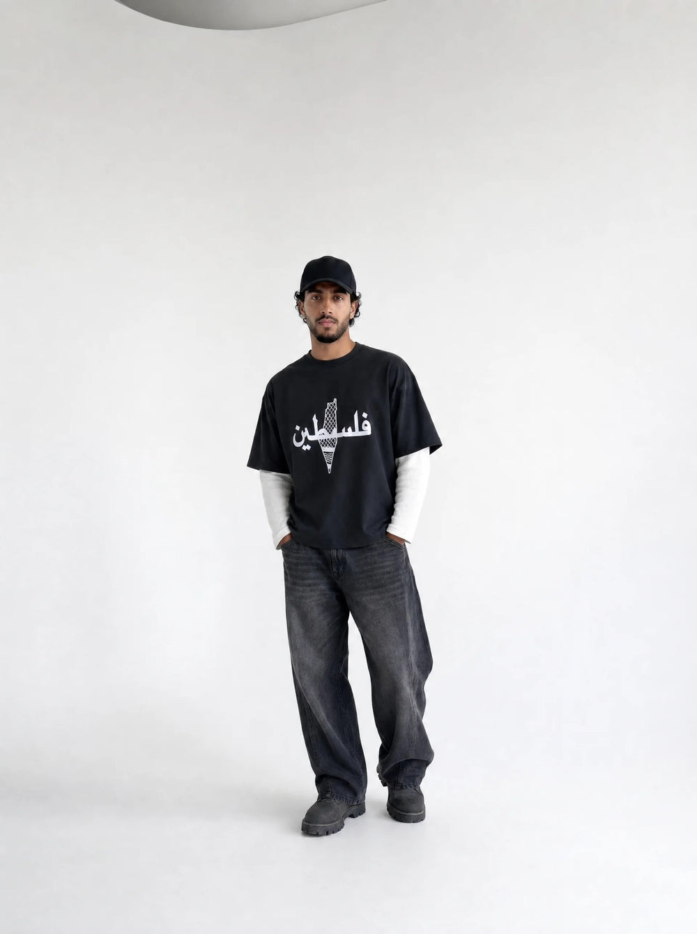 Person wearing a black t-shirt with white text and graphics, standing against a plain background