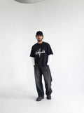 Person wearing a black t-shirt with white text and graphics, standing against a plain background